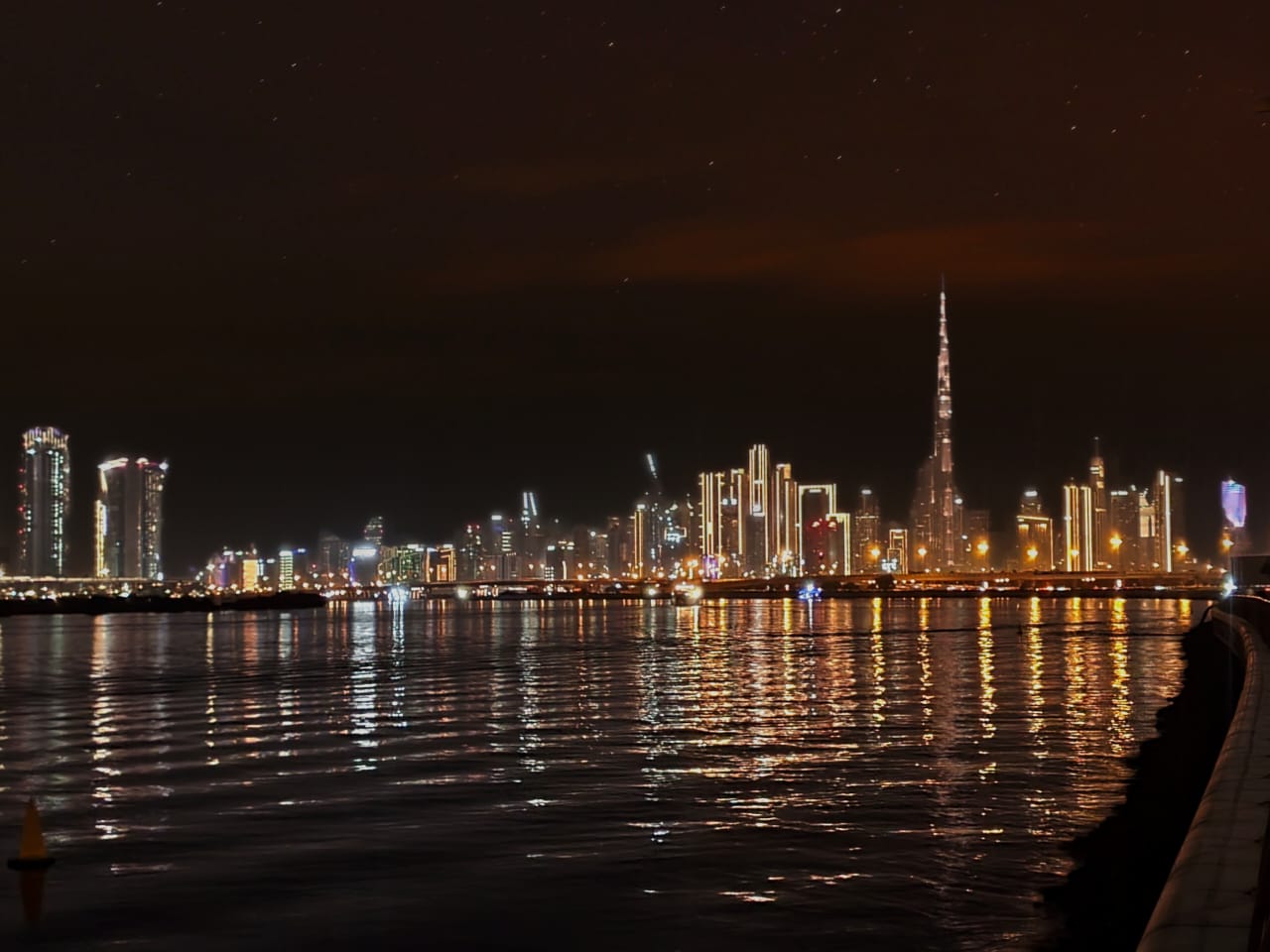 Illuminated Dubai skyline and Burj Khalifa reflected in water, taken from Al Jaddaf.